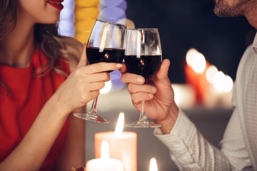 Couple toasting with red wine glasses in a romantic candlelit setting, with warm lights and a cozy ambiance in the background.