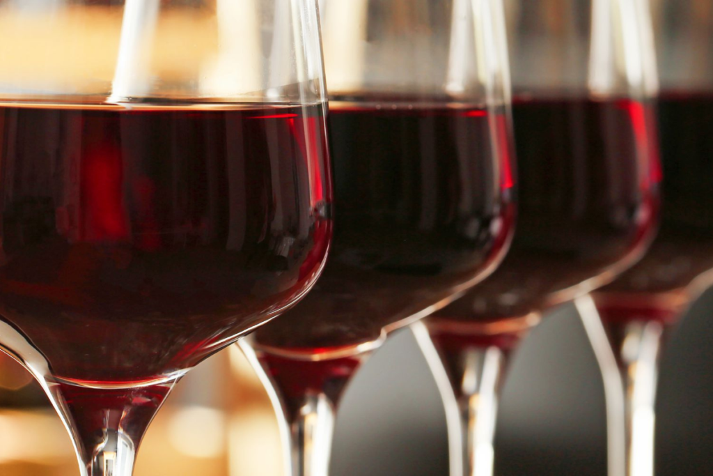 Close-up of four glasses filled with red wine, capturing the deep red hues and reflections on the glass, set against a warm background.