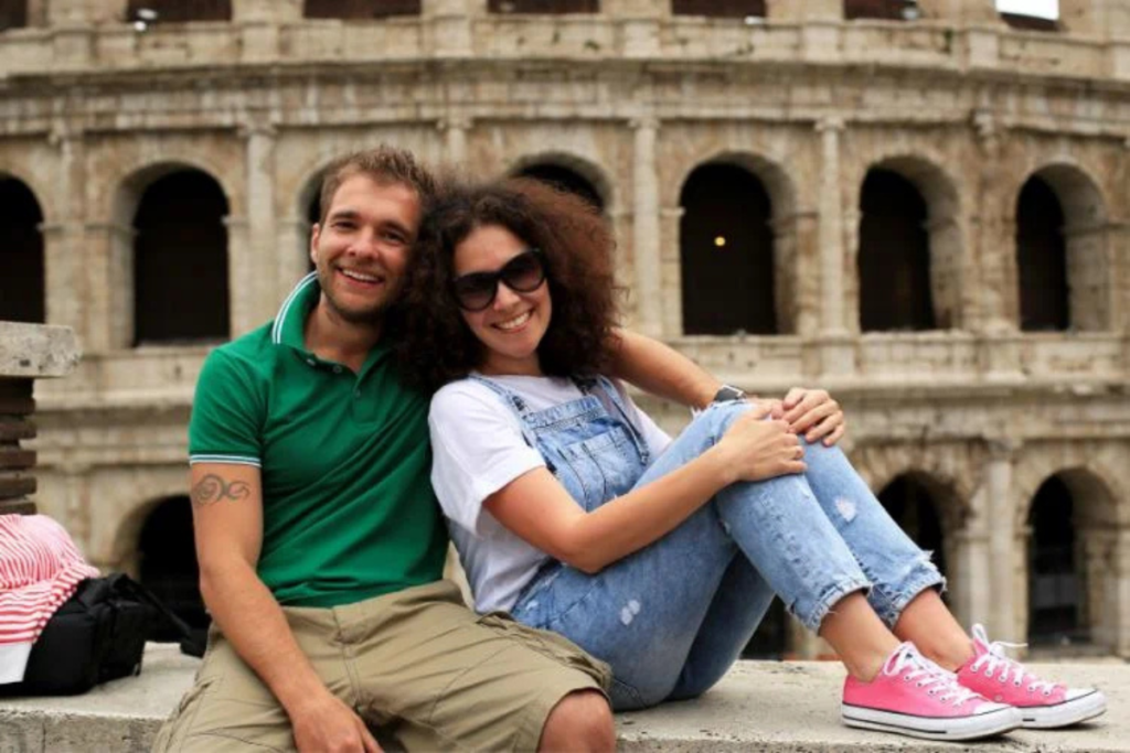 Happy couple sitting together in front of the Colosseum, smiling and enjoying their trip.