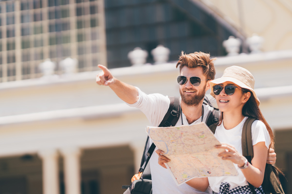 Happy tourist couple with a map, man pointing ahead, exploring a city on a sunny day.