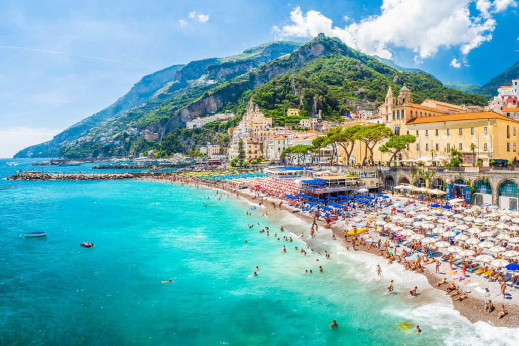 Sunny beach scene on the Amalfi Coast, with turquoise waters, colorful umbrellas, and lush cliffs.