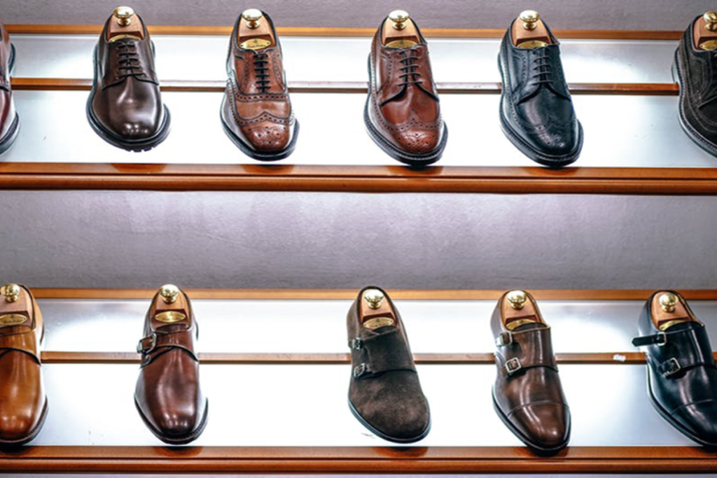 Assorted men's dress shoes in brown and black displayed on illuminated wooden shelves.