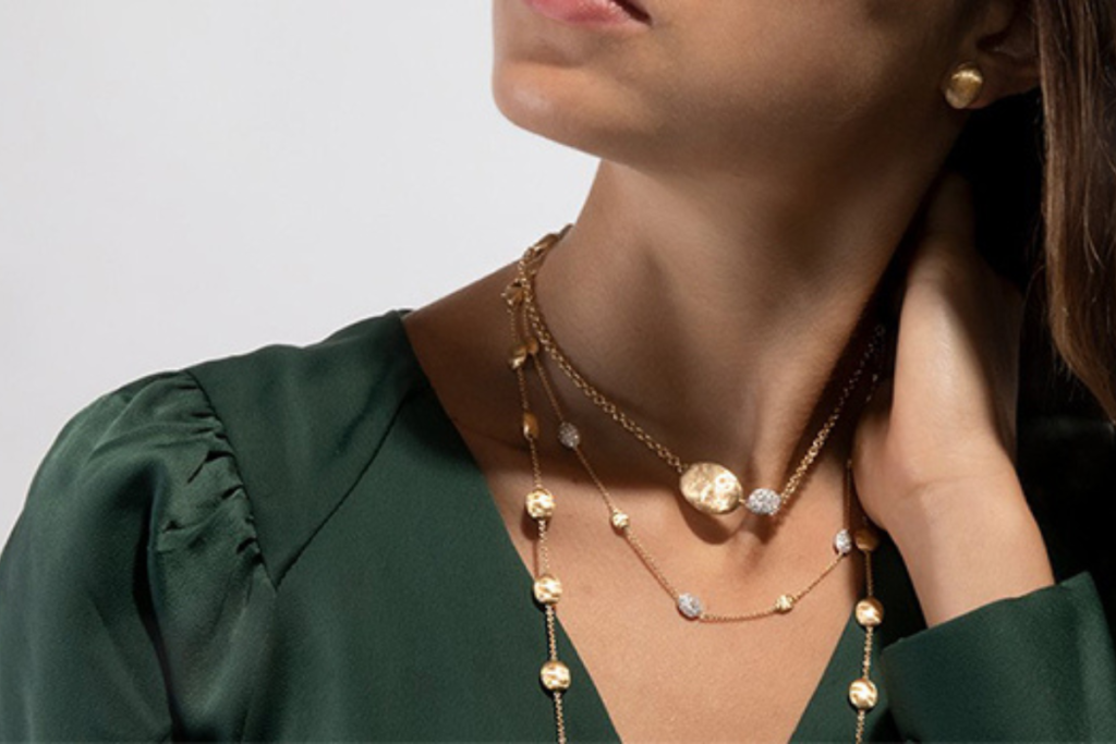 Elegant woman wearing layered gold necklaces with textured pendants and matching earrings, dressed in a dark green blouse.