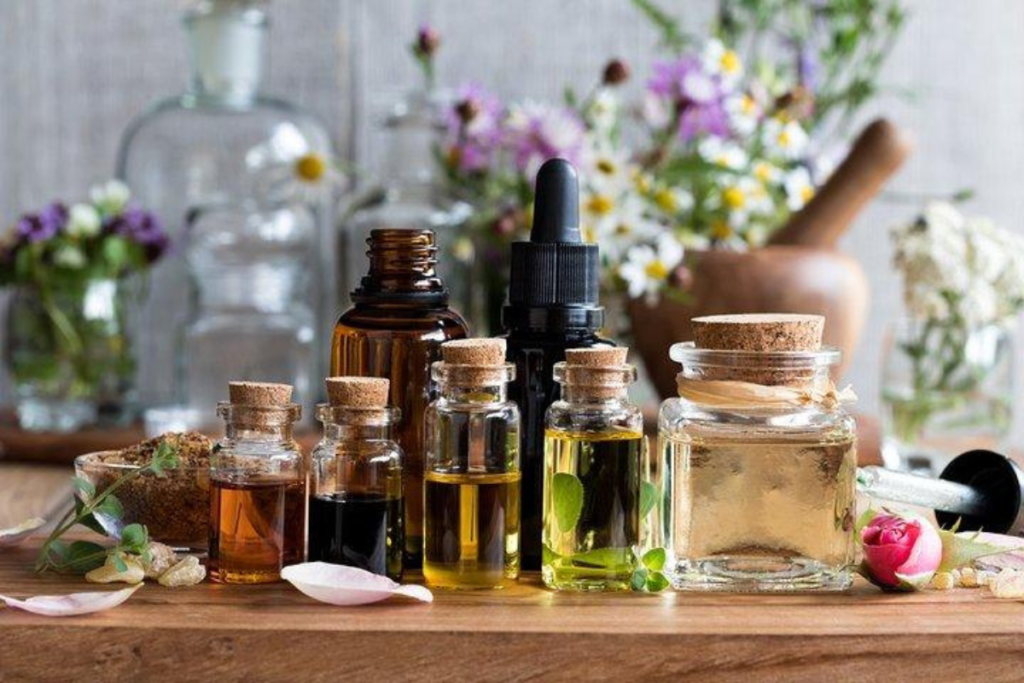 Assorted essential oil bottles with cork lids on a wooden table, surrounded by herbs and flowers.