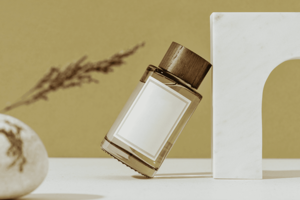 Minimalist perfume bottle with wooden cap leaning against a white marble stand on a beige background.