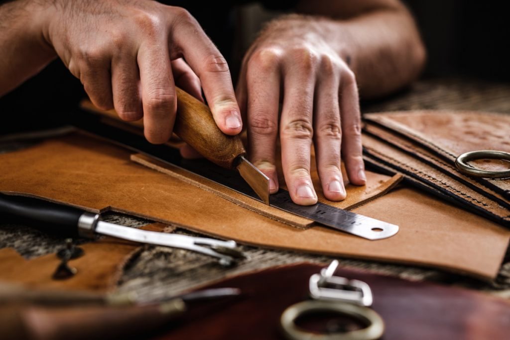 Close-up of artisan hands cutting leather with a tool and ruler, crafting a handmade item.