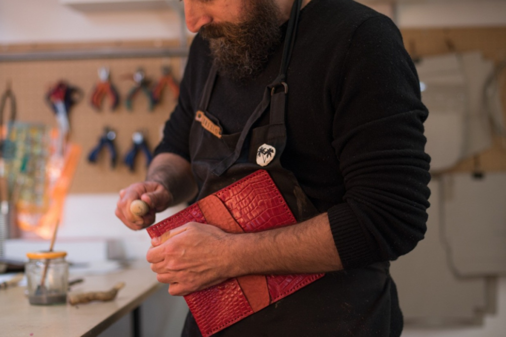 Artisan working on a textured red leather piece in a workshop, using hand tools for detailing.