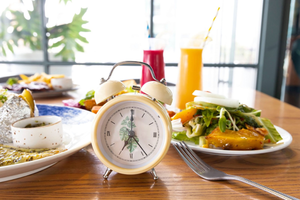 Table with a variety of healthy meals and drinks, featuring a vintage clock as a focal point, symbolizing meal timing and mindful eating.