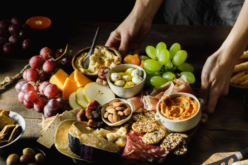 Charcuterie board with grapes, cheese, hummus, olives, nuts, crackers, and spreads, artistically arranged with a variety of fruits.