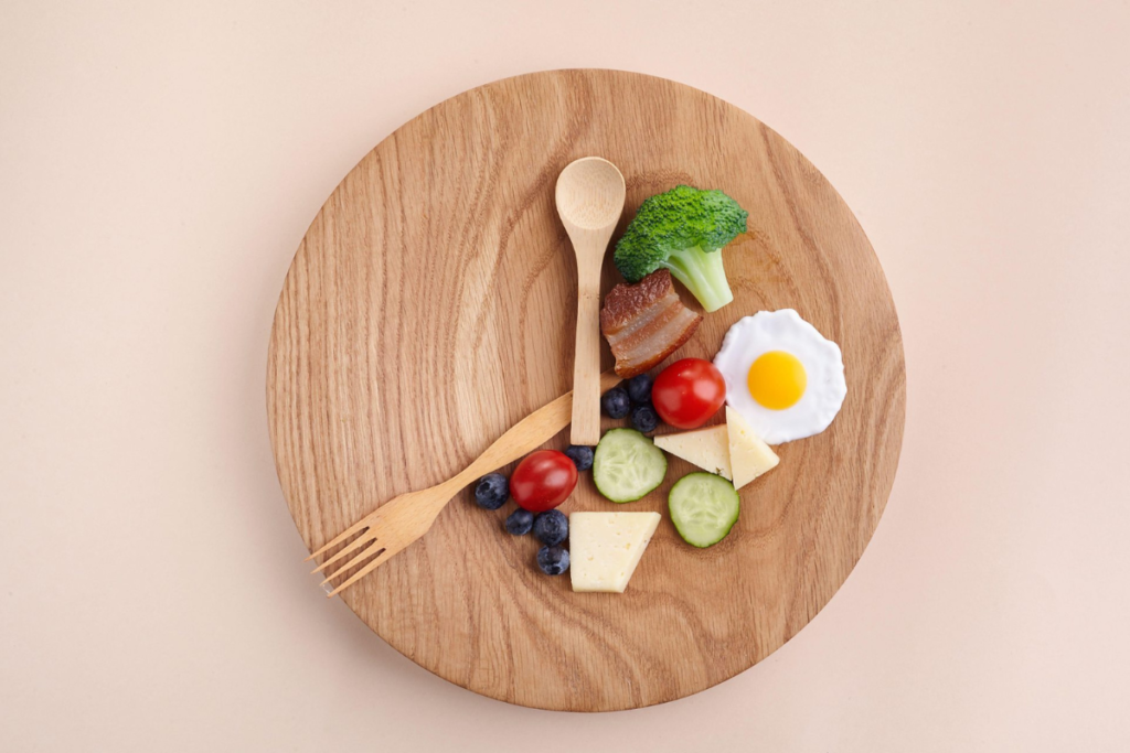 Minimalistic wooden plate with a small serving of food including broccoli, cherry tomato, cucumber, cheese, blueberries, and a sunny-side-up egg.