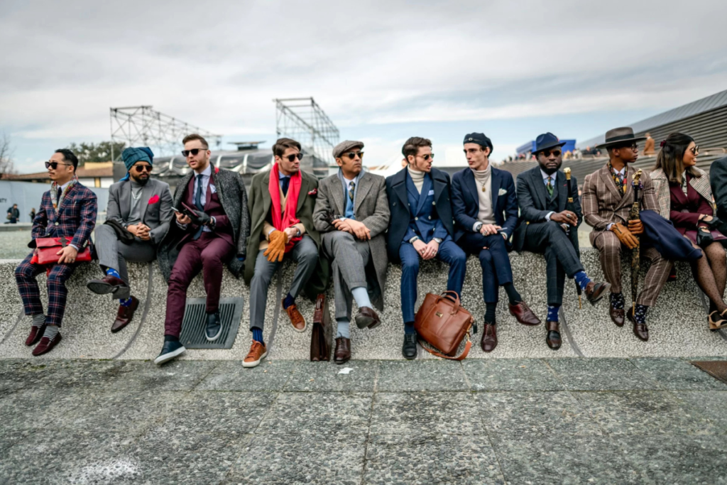 Group of stylishly dressed men in diverse suits sitting outdoors, showcasing unique fashion styles.