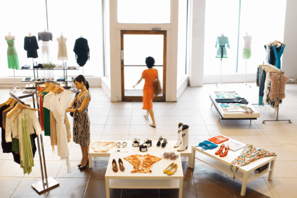 Modern clothing store interior with mannequins, clothing racks, and accessories on display tables.