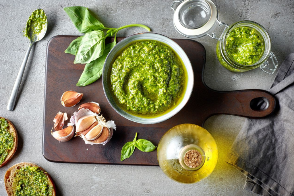 Bowl of fresh basil pesto on a wooden board with garlic cloves, olive oil, and basil leaves, perfect for a flavorful Italian dish.